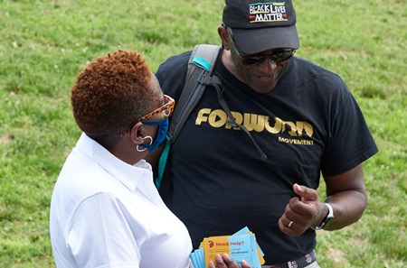 Armenta Washington, MS, senior research coordinator, holds cards about health information while speaking with a man wearing a Black Lives Matter cap.